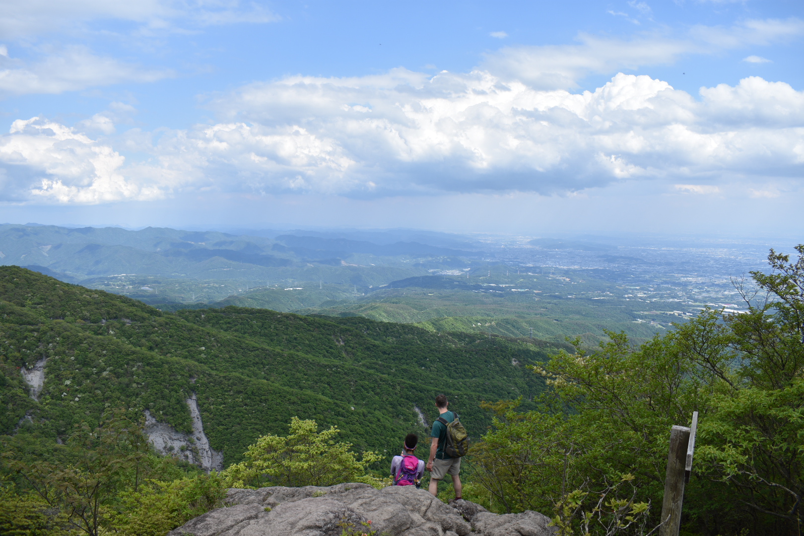 2 hikers looking out at a view of mountains and towns in the distance from Hisashi Iwa, Mt. Akagi