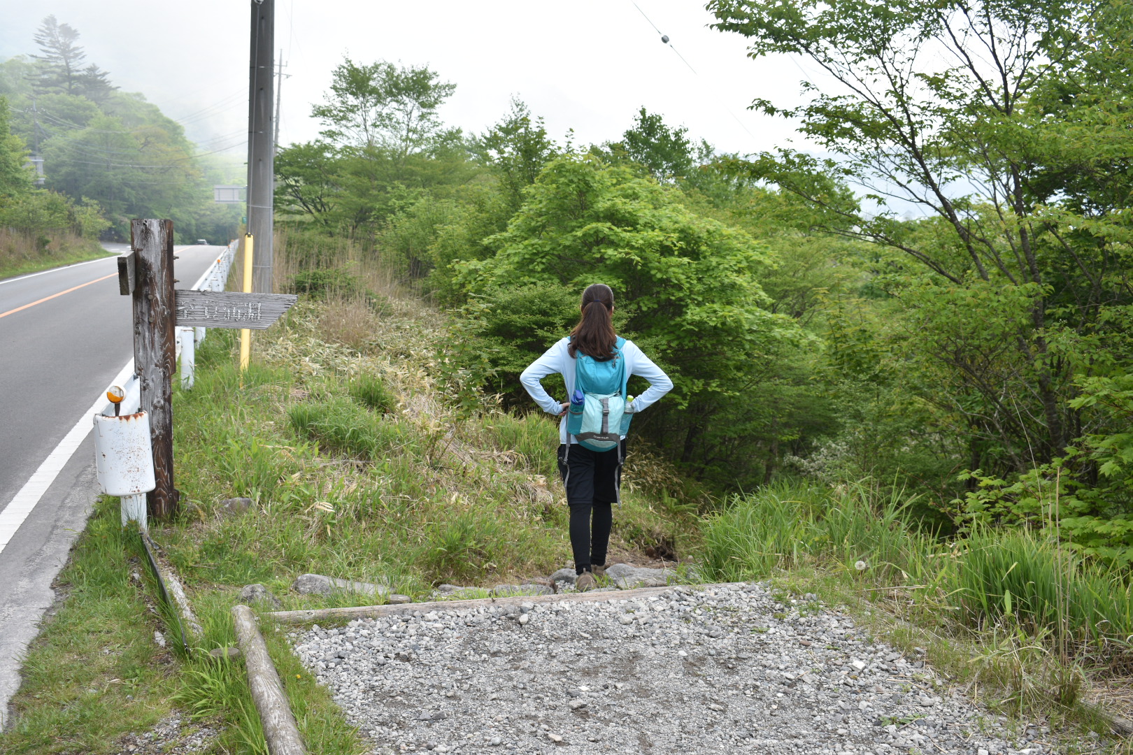 A hiker descends down a gravel trail next to a paved road