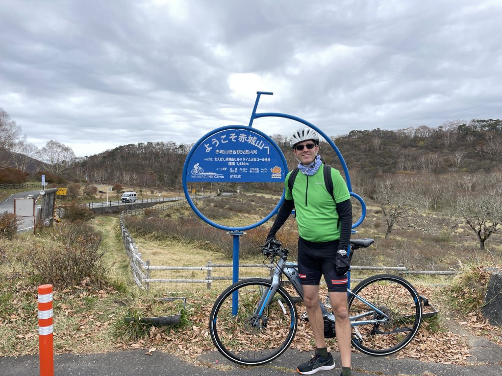 A man standing with a bicycle in front of the Akagi Hill Climb goal signboard
