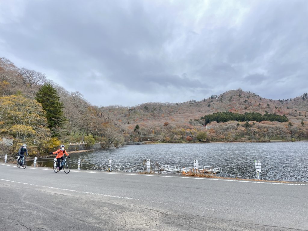 Cyclists wearing windbreakers riding past a lake