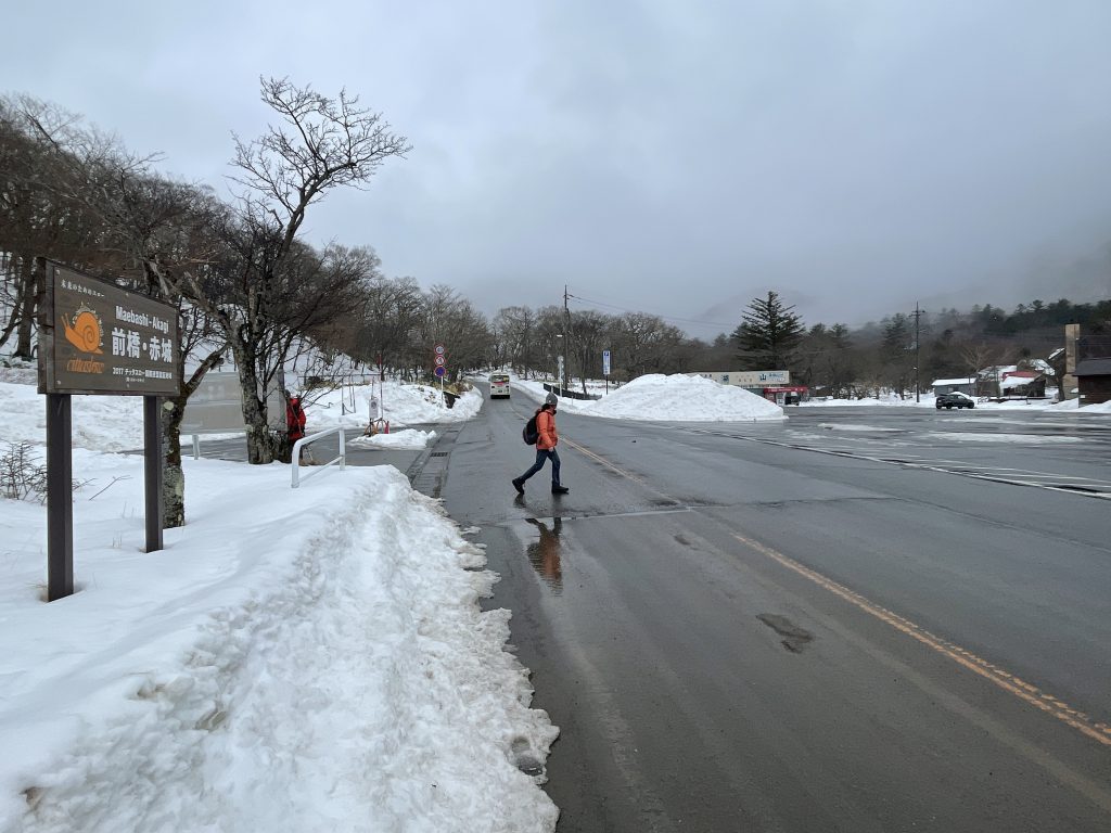 A woman walking across the street on a snowy mountain at Akagi Hiroba Mae bus stop