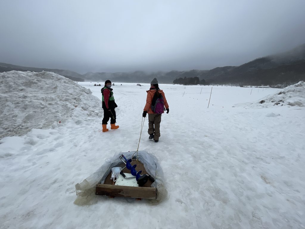 Two people pulling ice fishing equipment onto frozen Lake Onuma on Mt. Akagi