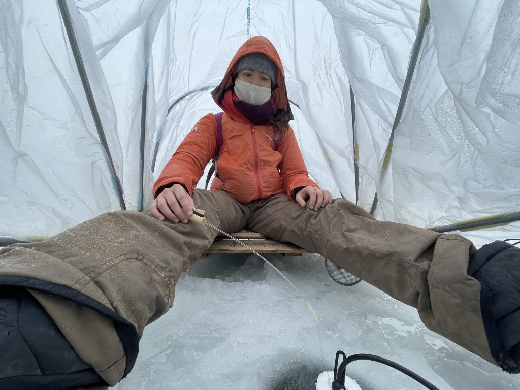 A woman ice fishing inside a tent